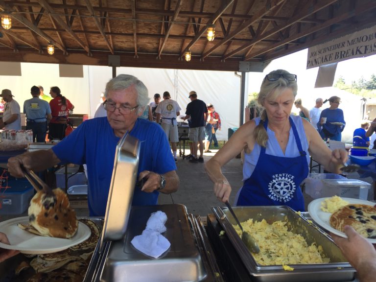 Two people serve eggs and pancakes wearing Rotary Service clothes